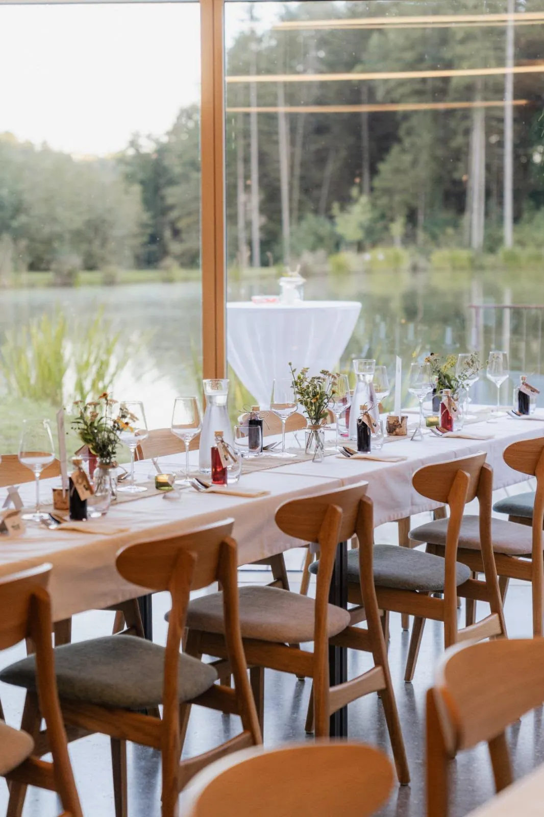 Festlich gedeckter Tisch mit Blick auf Teich und Wald durch große Fenster